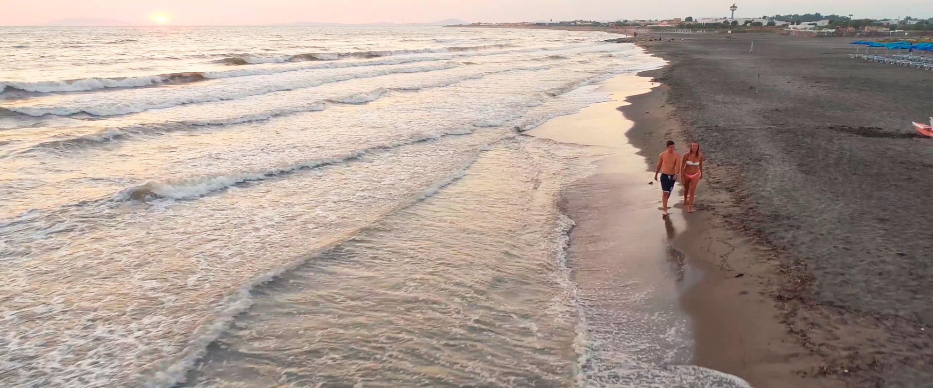 Coppia cammina sulla spiaggia al tramonto, onde leggere e cielo sereno.