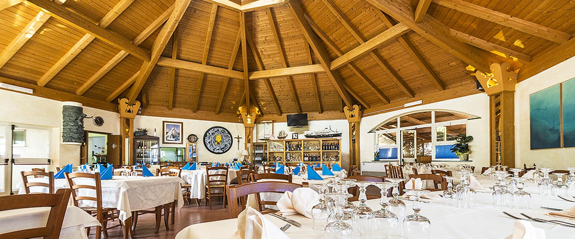 Ristorante con soffitto in legno, tavoli apparecchiati elegantemente, atmosfera accogliente e luminosa.