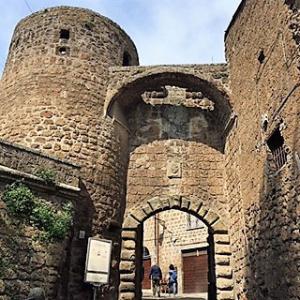 Antico arco in pietra, ingresso a un borgo medievale con torri fortificate.