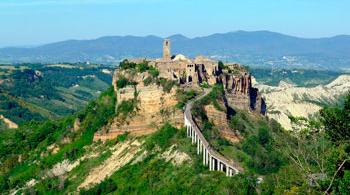 Antico borgo su una collina, accessibile tramite un ponte, circondato da paesaggi verdi.