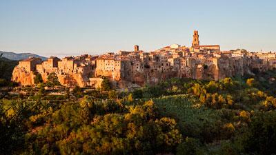 Città medievale su una collina, circondata da paesaggi verdi e alberi.