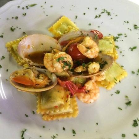 Ravioli di pesce con gamberi, vongole e pomodorini, guarniti con prezzemolo.