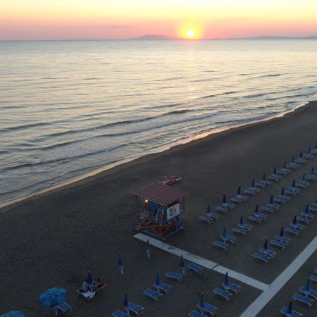 Spiaggia al tramonto con ombrelloni e sdraio allineati, mare calmo e torretta.