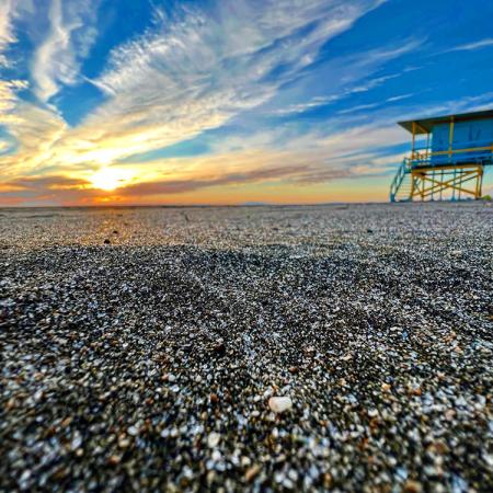 Spiaggia al tramonto con torretta di salvataggio e cielo nuvoloso.