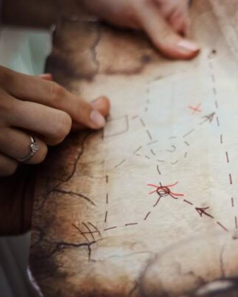 Mani che tengono una mappa antica con percorsi segnati da linee tratteggiate.