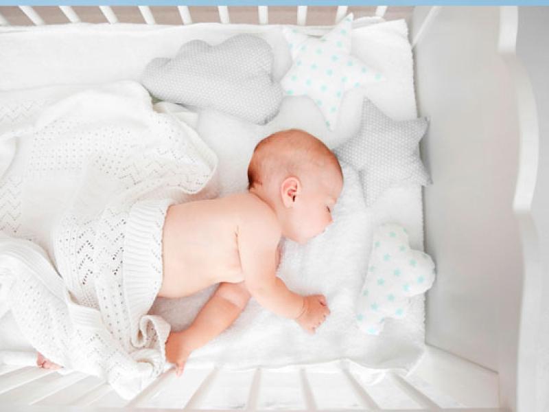 Neonato che dorme in culla con cuscini a forma di stella e nuvola.