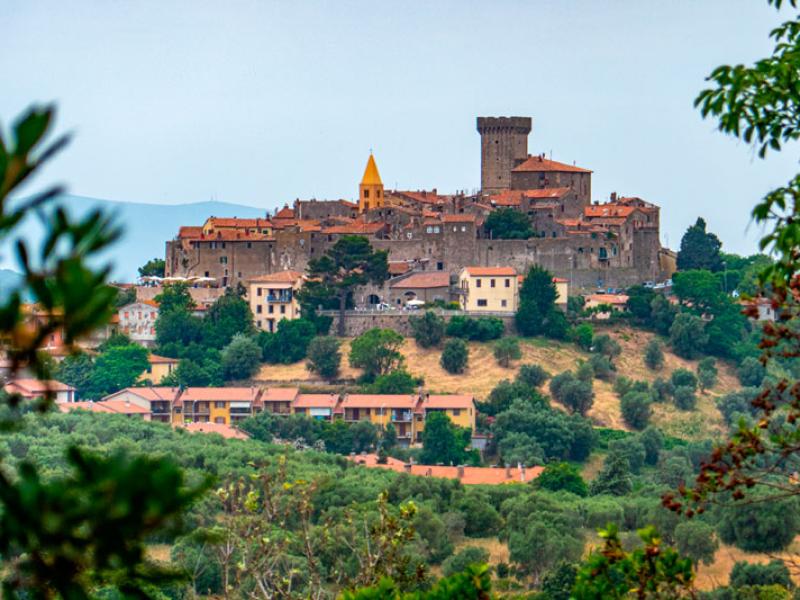 Borgo medievale con torre e chiesa, circondato da colline verdi.