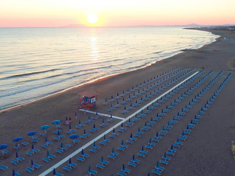 Spiaggia al tramonto con ombrelloni blu allineati e mare calmo.